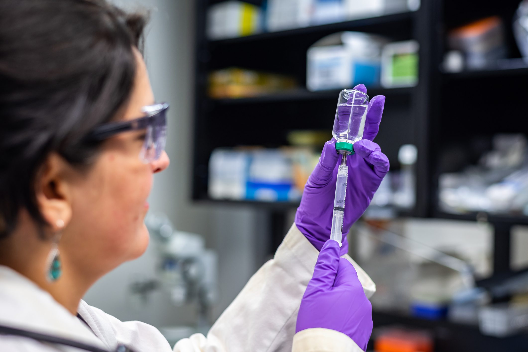 Researcher in lab drawing liquid from a vial with a syringe