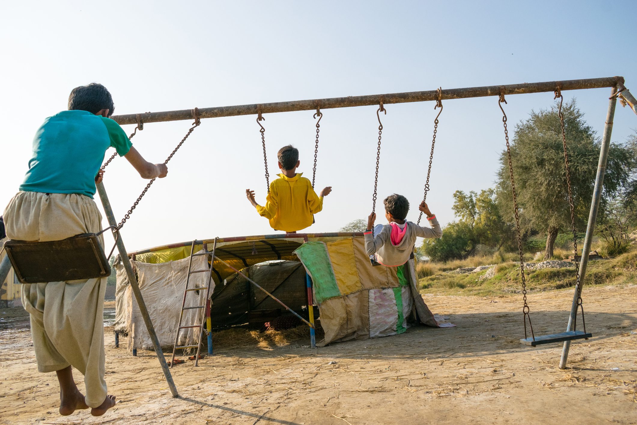 Children and woman playing on swings in a dry desert area